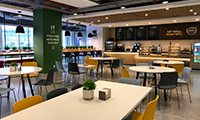 Bright modern cafe interior with white tables, wooden chairs, a service counter, and large windows for natural light.