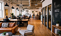 Cozy cafe interior with wooden floors and exposed ceiling beams, customers seated at tables and a bar area in the background.