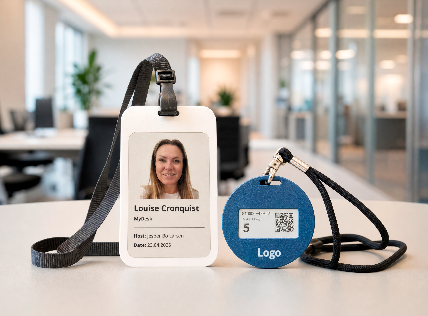 Employee ID badge on a desk showing Louise Cronquist’s photo and details, with a blue circular security tag beside it in a bright office setting.